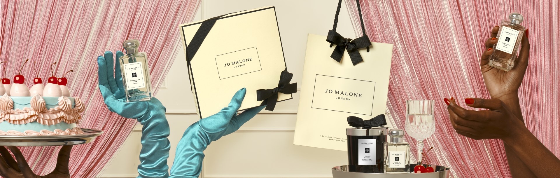 birthday cake & a pair of hands in satin green gloves holding jo malone gift bags, gift boxes, candle and diffuser